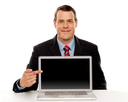 Seated young businessman pointing at blank laptop screen. Laptop facing camera