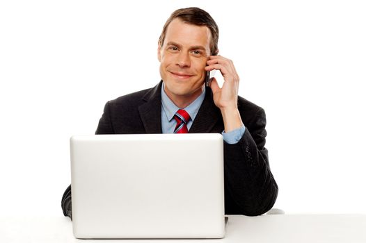 Businessman sitting in front of laptop on work desk and talking on cell phone