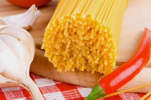 Golden raw dried Italian pasta with other ingredients on kitchen desk.