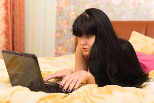 Concentrated young woman with a laptop in bed