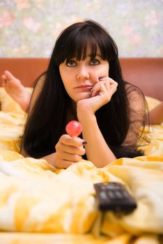 Sad woman with candy and TV remote control unit in bed