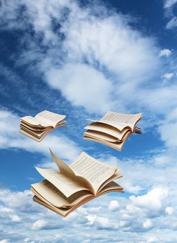 Three open books flying on blue sky background fantasy