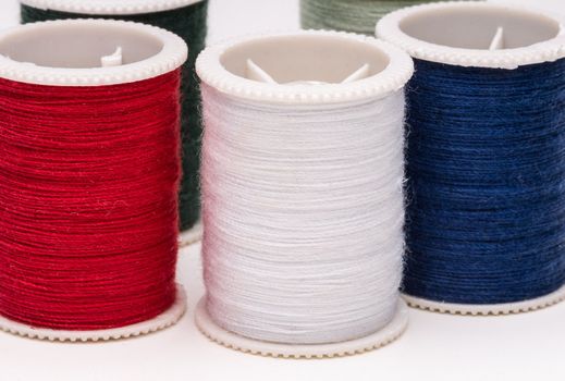 Clos-up of colored spools of string on white background.