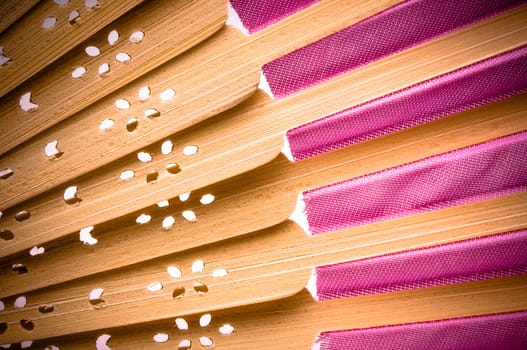 Close-up of a pink wooden hand made fan on white.