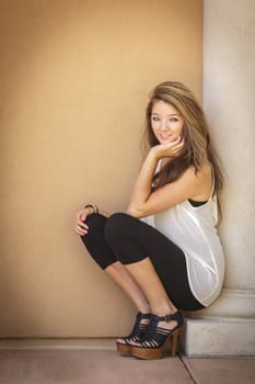 Attractive Mixed Race Girl Portrait Sitting Outdoors Against Wall.