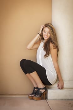 Attractive Mixed Race Girl Portrait Sitting Outdoors Against Wall.