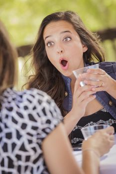 Attractive Shocked Girl Talking with Friend Over Drinks Outdoors.