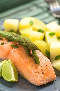 Baked salmon fillet with green asparagus, lime wedges and boiled potatoes (Selective Focus, Focus on the tip of the asparagus heads on the top and on the right)