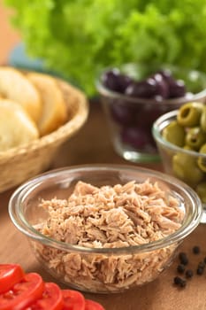 Canned tuna in glass bowl with fresh salad ingredients (olives, tomato, lettuce) and bread (Selective Focus, Focus one third into the tuna) 