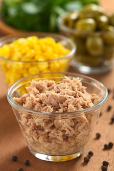 Canned tuna in glass bowl with fresh salad ingredients (sweet corn, green olives and watercress) in the back (Selective Focus, Focus one third into the tuna) 