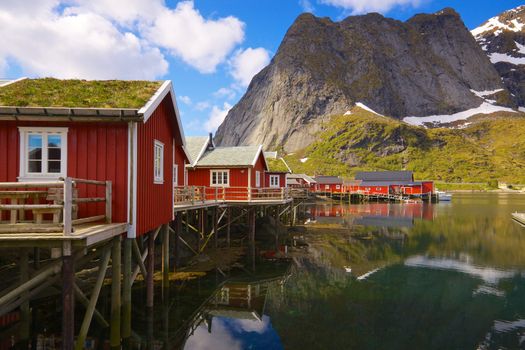 Typical red rorbu fishing huts with sod roof on Lofoten islands in Norway reflecting in fjord