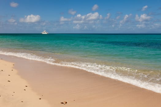 Tropical Caribbean Beach Seascape with Motor Yacht Sailing into the Distance on Beautiful Sunny Day