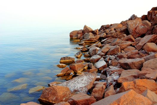 Stony coast leaving for horizon with blue sea water