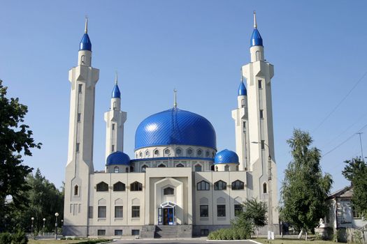 White mosque with blue domes against an unflawed sky