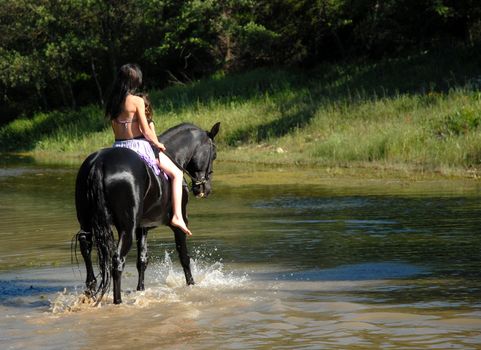 young woman and her stallion riding in a river