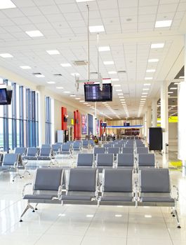 Airport lounge with chairs, tv screens, and windows