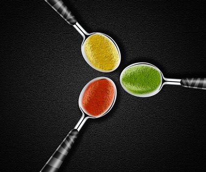 Collection of green, yellow and red spices on spoons onblack background