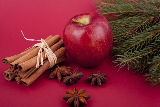 christmas decoration aromatic red apple, cinnamon, anise and tree on red background