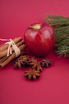 christmas decoration aromatic red apple, cinnamon, anise and tree on red background