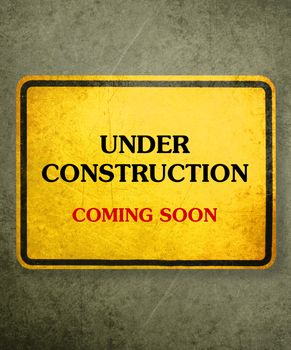 Alert yellow sign hanging on the wall, conceptual image for under construction and coming soon