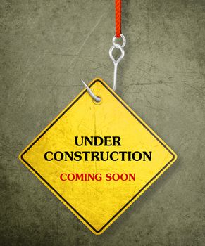 Alert yellow sign hanging by fishhook, conceptual image for under construction and coming soon
