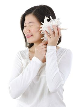 Asian female listening to a seashell over white background