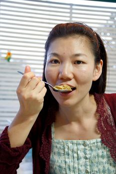 Asian lady is eating a spaghetti on a spoon