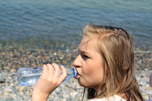 teenage girl drinking water sat on a beach