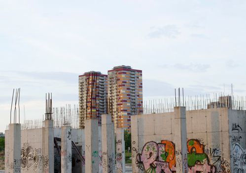 Unfinished building design painted graffiti and two tall skyscrapers in distance.