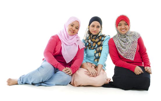 Portrait of three cheerful muslim women sitting on white background
