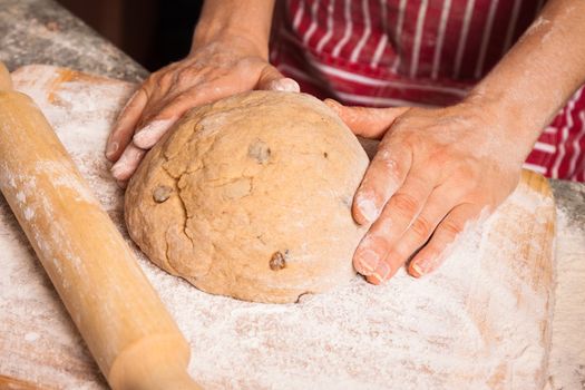 Close-up of hands on a bread dough with sultanas on a flour dusted chopping board.