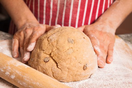 Close-up of hands kneeding a bread dough with sultanas on a flour dusted chopping board.