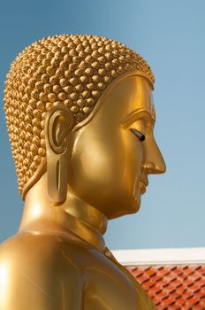 Buddha head in profile with blue clean sky and red temple roof on background