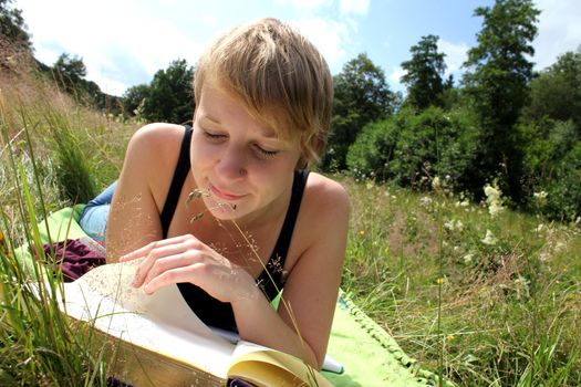 girl is reading a book on a summer meadow