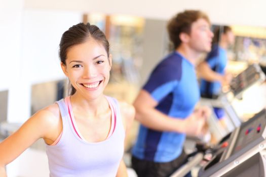 Fitness people portrait in gym. Woman smiling happy during running workout on treadmill in fitness center. Mixed race Cauasian / Chinese Asian female fitness model.