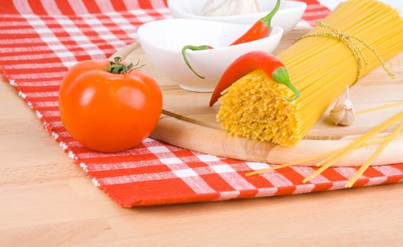 Golden raw dried Italian pasta with other ingredients on kitchen desk.