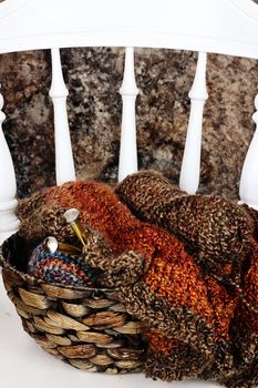 Basket filled with a crocheted blanket, soft skeins of yarn with needlework and knitting needles sitting on an old antique kitchen chair.