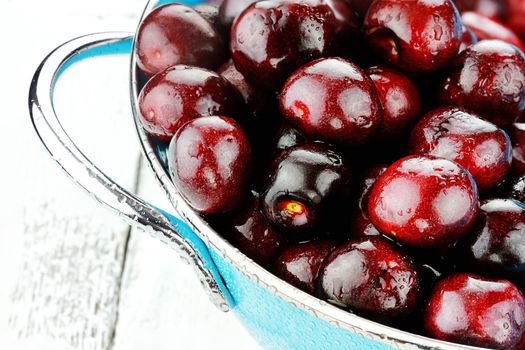 Blue colander filled with fresh black cherries over a rustic background.
