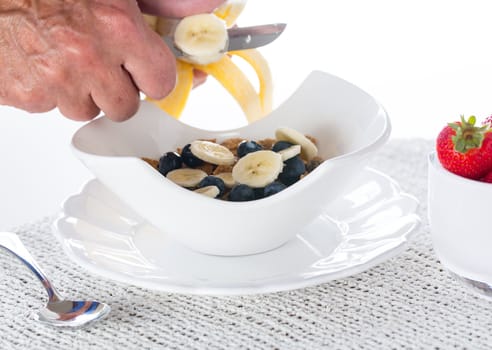 Breakfast of blueberries, bran flakes strawberries with banana being sliced