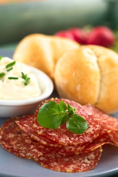 Thin salami slices garnished with watercress leaf with cream cheese and buns on plate (Selective Focus, Focus on the front of the watercress leaves)