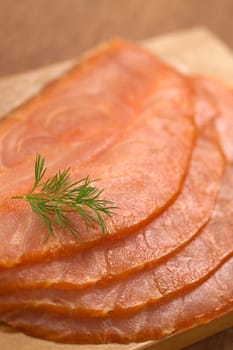 Thin smoked salmon slices with garnished with dill on wooden board (Selective Focus, Focus one third into the image)