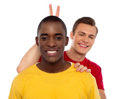 Guy making funny gesture behind his friends head isolated against white background