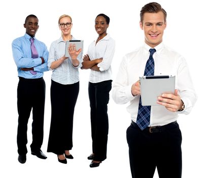 Handsome male executive operating tablet while colleagues discussing in background