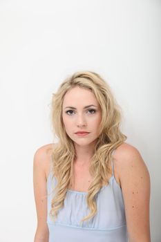 Doleful serious young blonde woman with hunched shoulders looking at the camera with copyspace on a white studio background