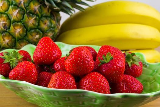 A bowl of fresh strawberries with pineapple and bananas