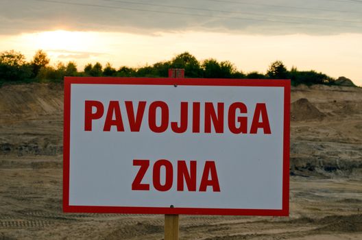 Lithuanian warning sign Danger Zone under construction site and sunset.