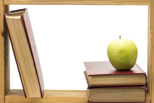 Some books with dark red hardcover and green apple in a wooden frame on white background