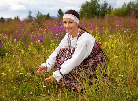 Young beautiful girl in national dress collects wild flowers 