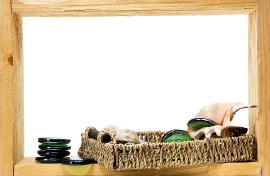 Wicker, green pieces of glass and sea shells inside rough wooden frame on white background