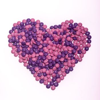 A bunch of chocolate buttons, in pink and purple in a heart shape, on a white background.